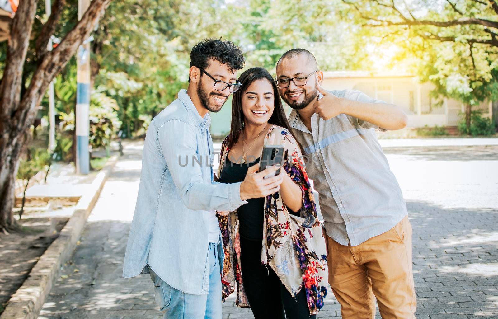 Happy friends watching a cell phone in the street. Three happy friends sharing the cell phone in the street. Concept of happy friends sharing media on a phone by isaiphoto