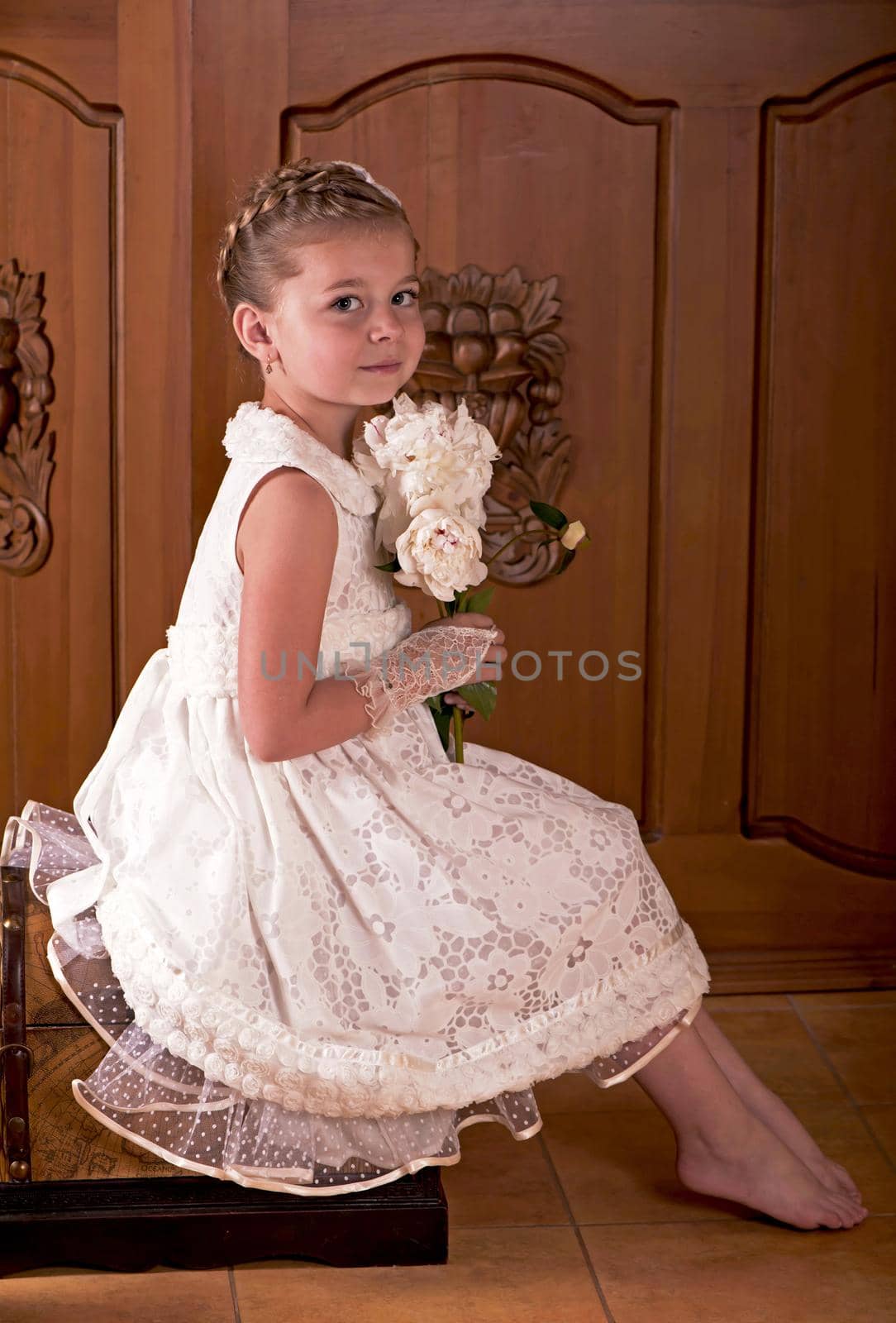 Children's holiday. Elegant girl in a white dress. Girl holding fresh peonies bouquet on wooden background by aprilphoto