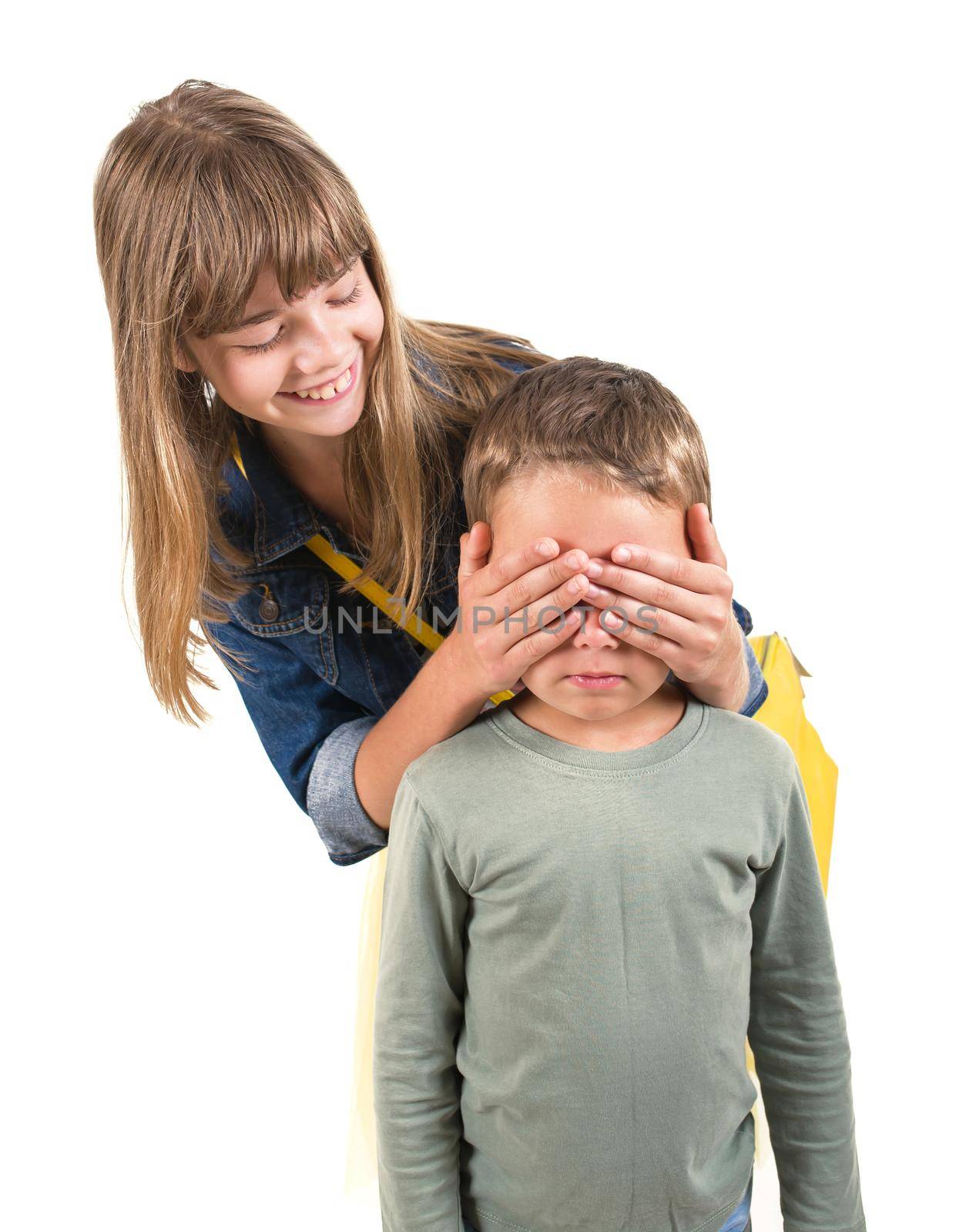 Teen boy covering girl's eyes to surprise her. Portrait of brother and sister isolated on white background. Funny couple children laughing with a perfect smile.