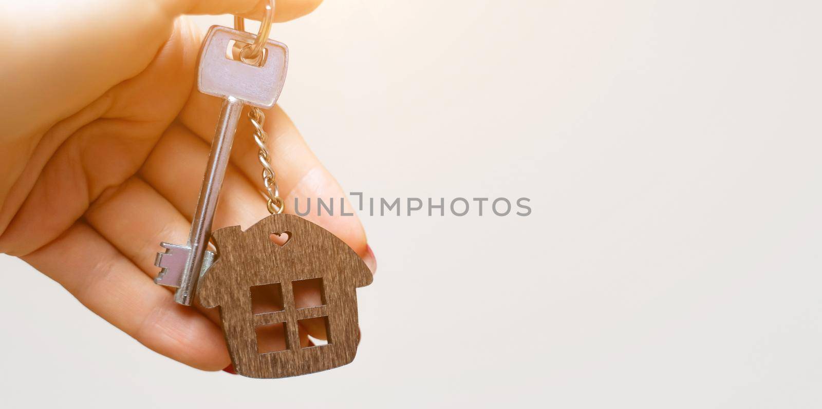 A woman's hand holds a house key on a white background with copy space. Real estate agent. Buying a house, apartment