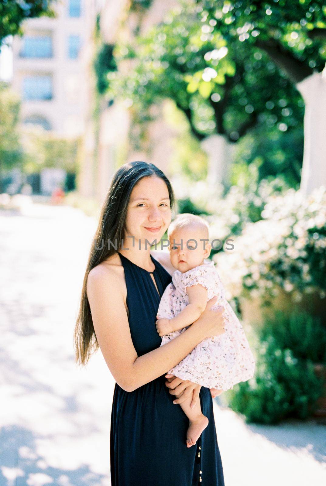 Mom with a little baby girl in her arms stands on the street by Nadtochiy