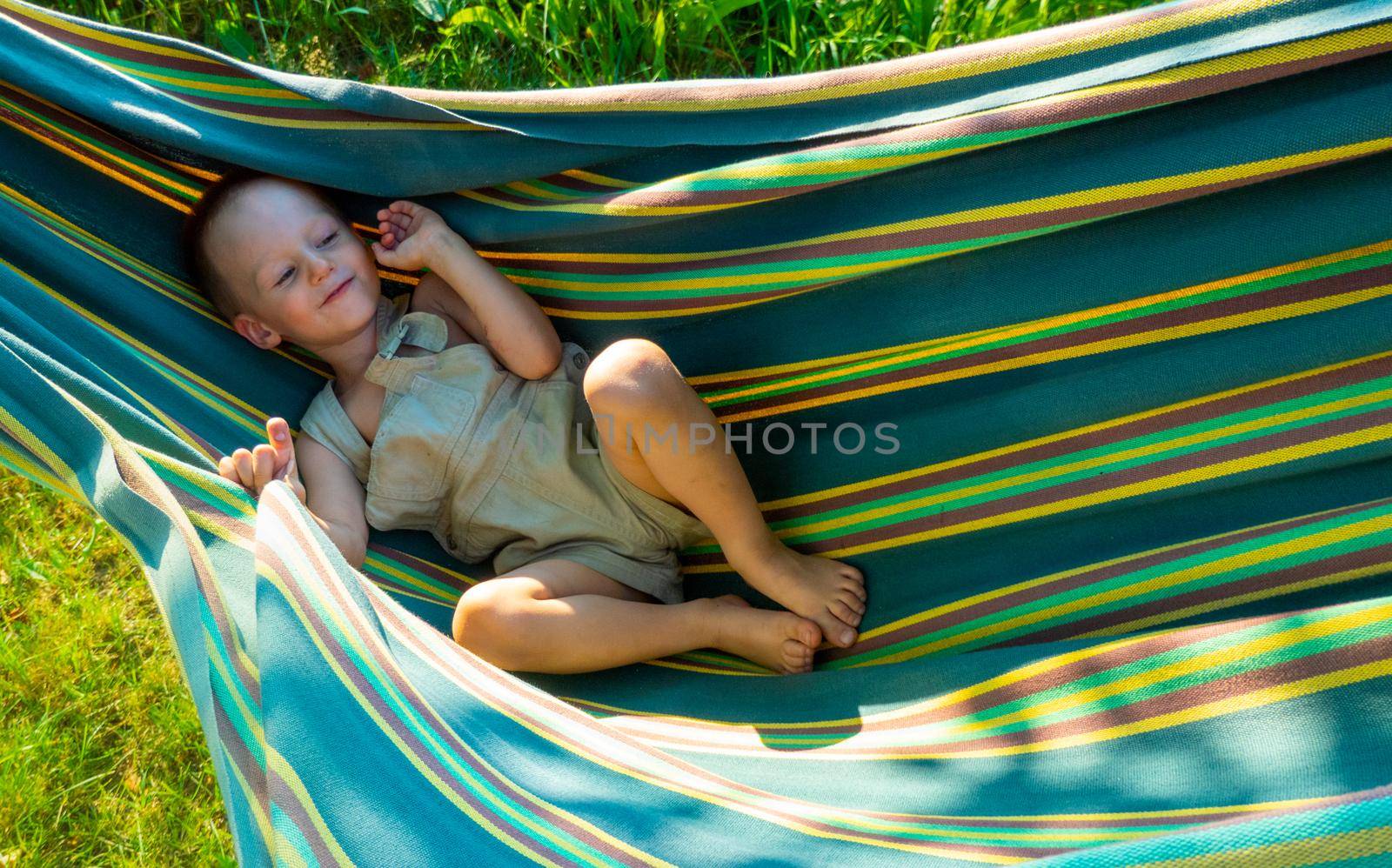 Cute little blond caucasian boy having fun with multicolored hammock in backyard or outdoor playground. Summer active leisure for kids. Child on hammock. Activities and fun for children outdoors. High quality photo