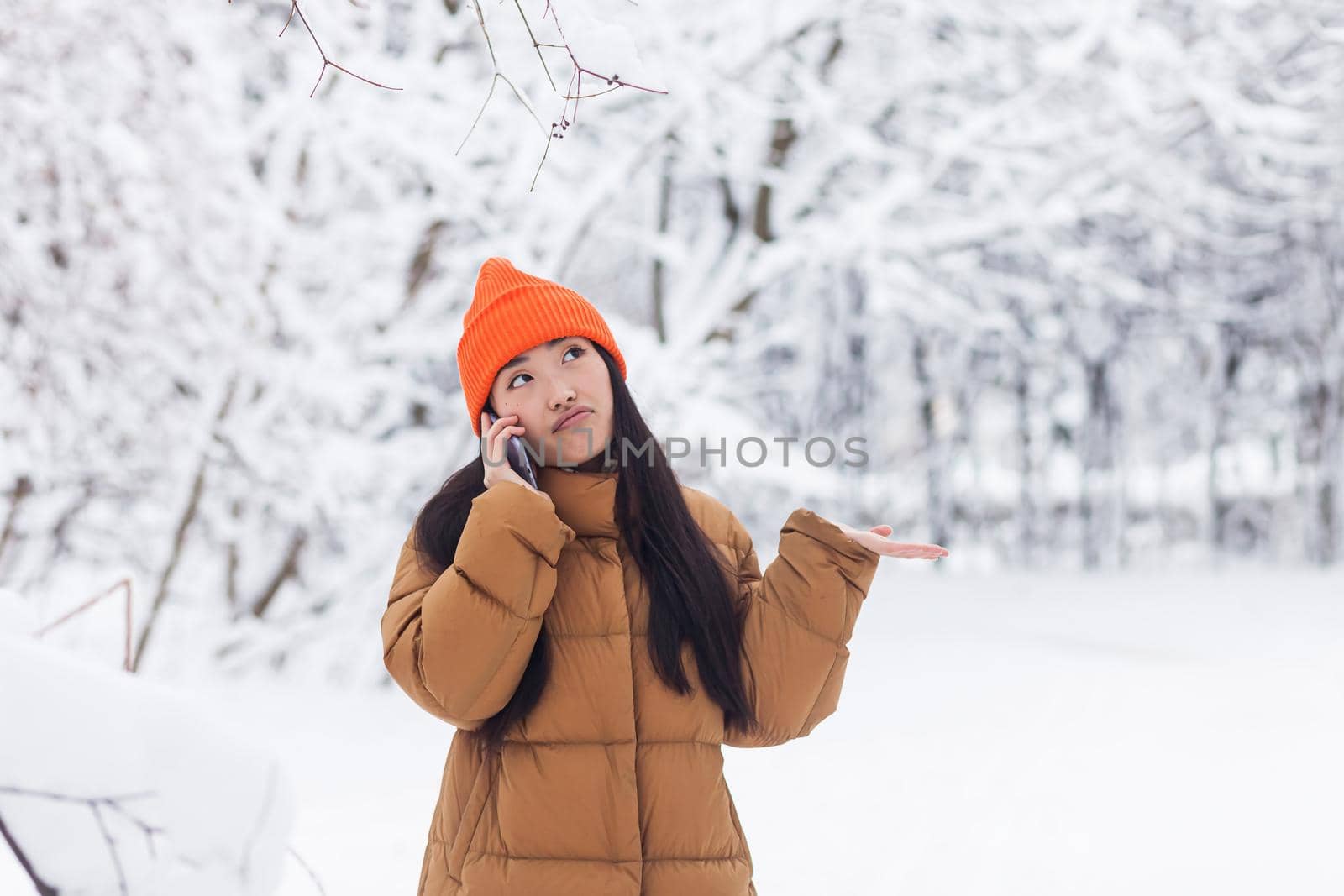 Beautiful asian woman in warm clothes talking on the phone in the park on a winter snowy day on a walk
