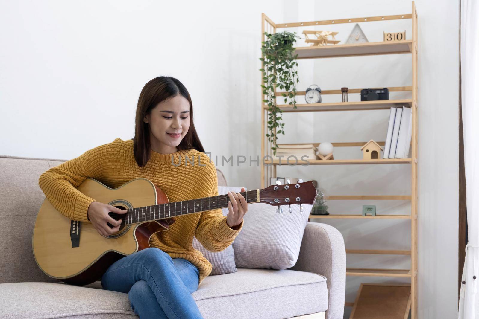 Inspired young woman composing song on acoustic guitar at home by wichayada