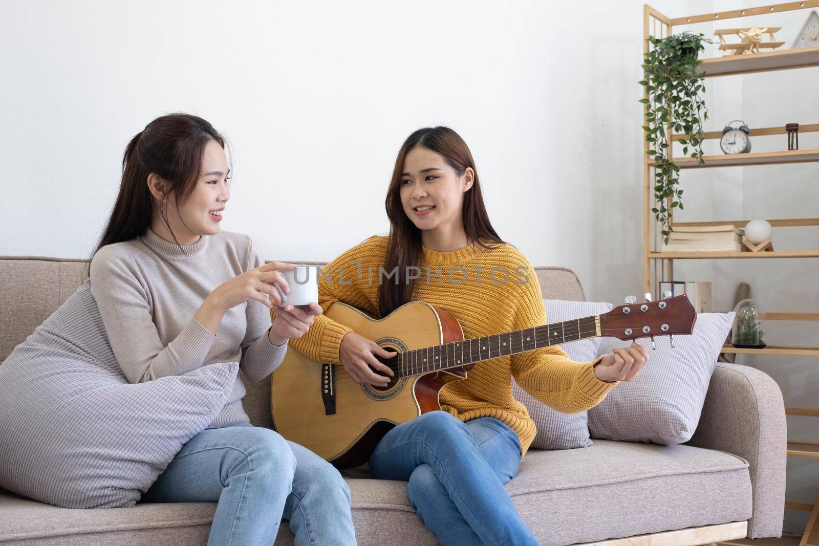 A young woman playing guitar on the sofa in the living room. Young Asian loving lovers couple bonding at home, relaxing on sofa the living room..