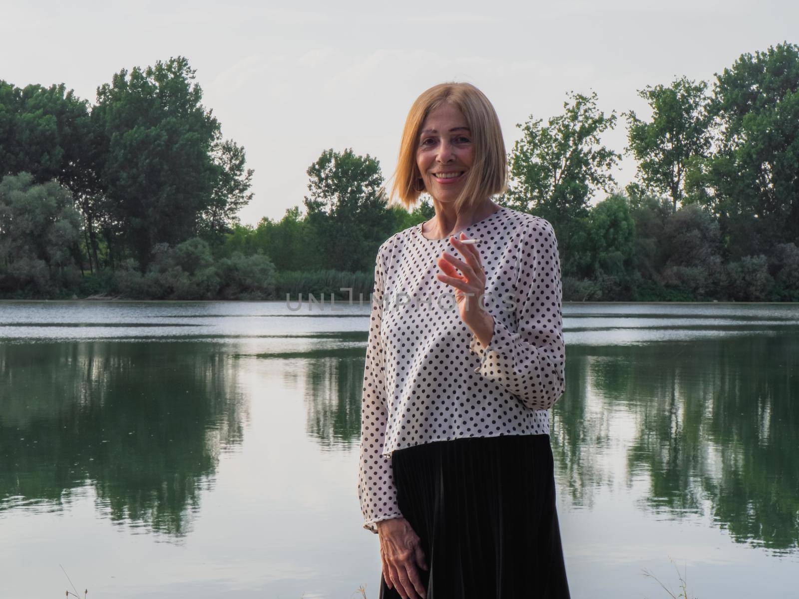 female pensioner having fun and smoking a cigarette in a park - aging free and wellness concept