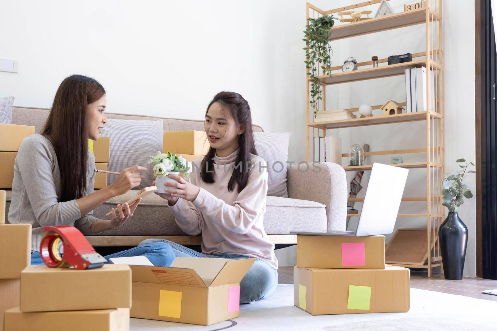 Startup small business owner working with computer at workplace. Freelance two woman seller check product order. Packing goods for delivery to customer. Online selling. E-commerce. Online Shopping by wichayada