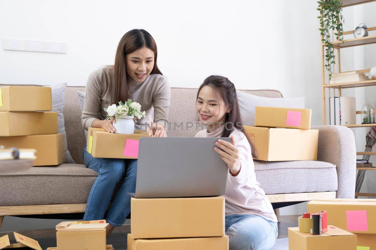 Startup small business owner working with computer at workplace. Freelance two woman seller check product order. Packing goods for delivery to customer. Online selling. E-commerce. Online Shopping.