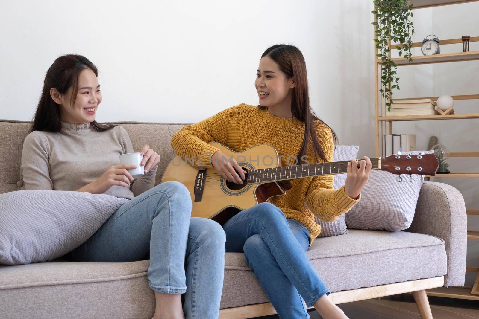 Asian girl friends play guitar together in the living room at home