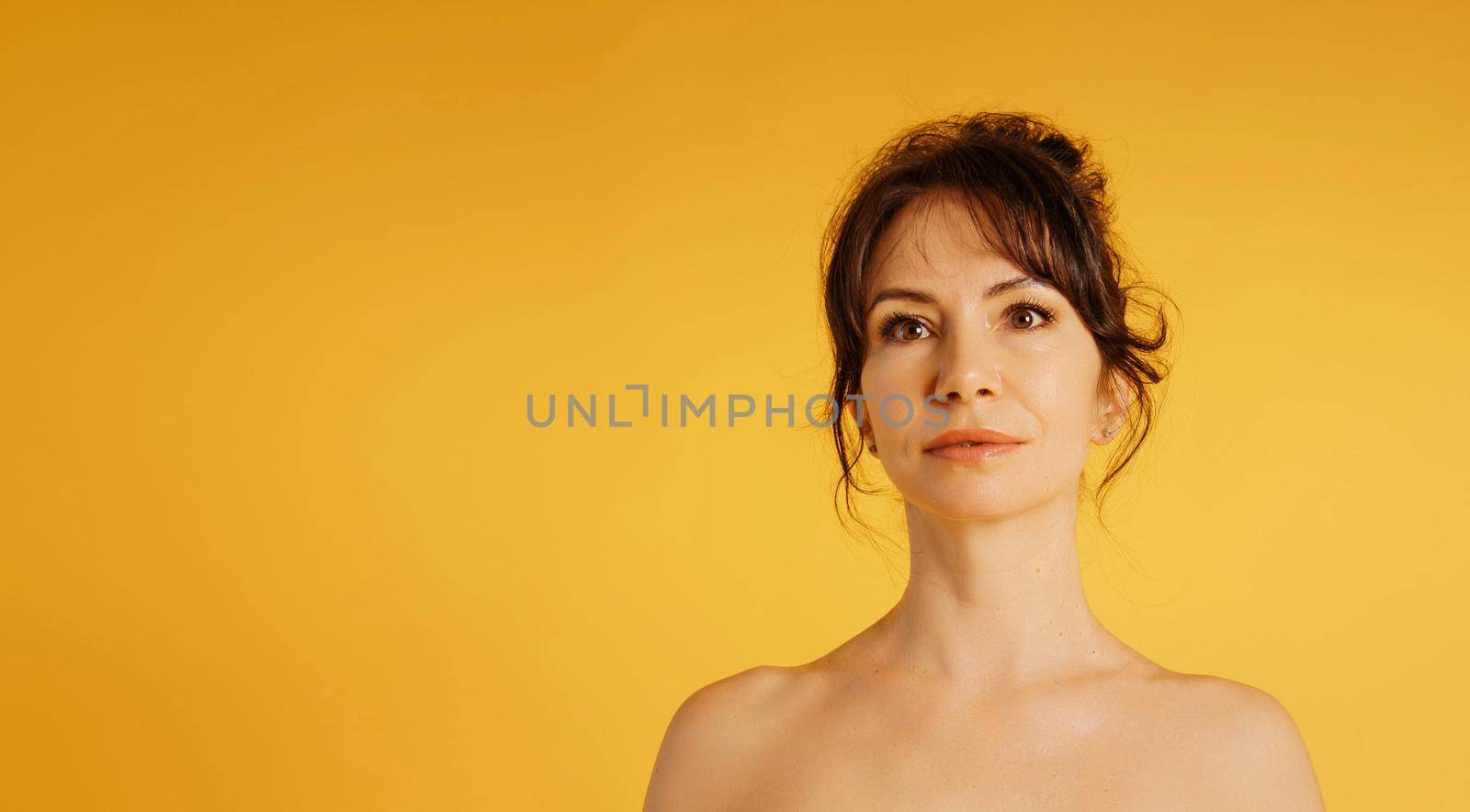 Portrait of a beautiful middle-aged woman in a yellow dress, her hair pulled up against a yellow background.