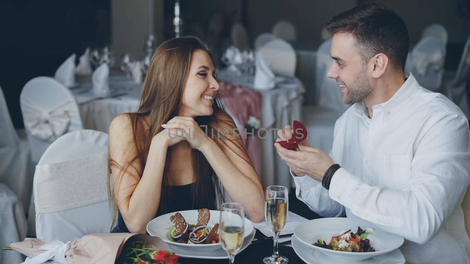 Attractive young woman is saying yes to marriage proposal. Romantic relationship and restaurant date concept by silverkblack