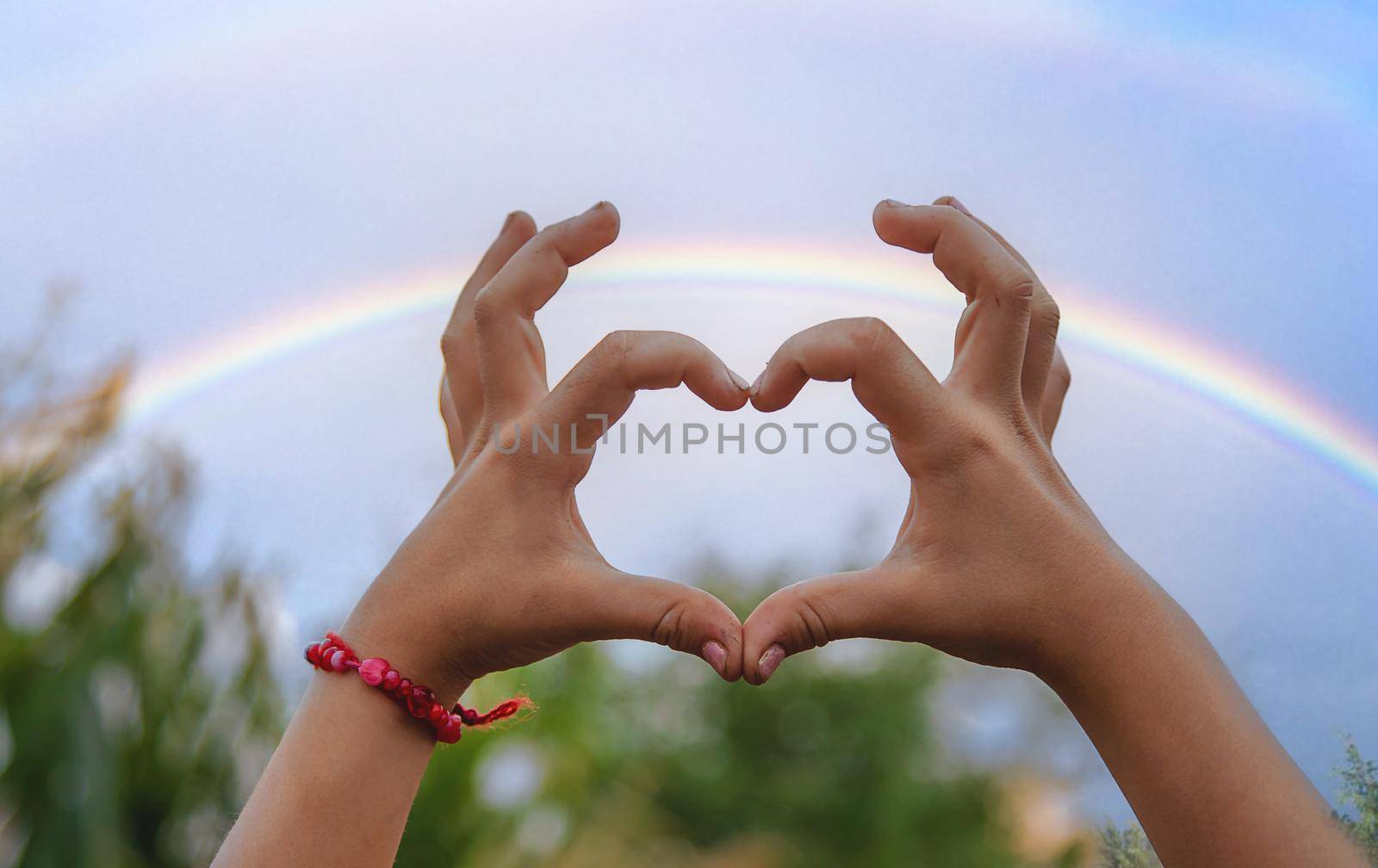 The child makes a heart with his hands rainbow, . Selective focus. Kid.