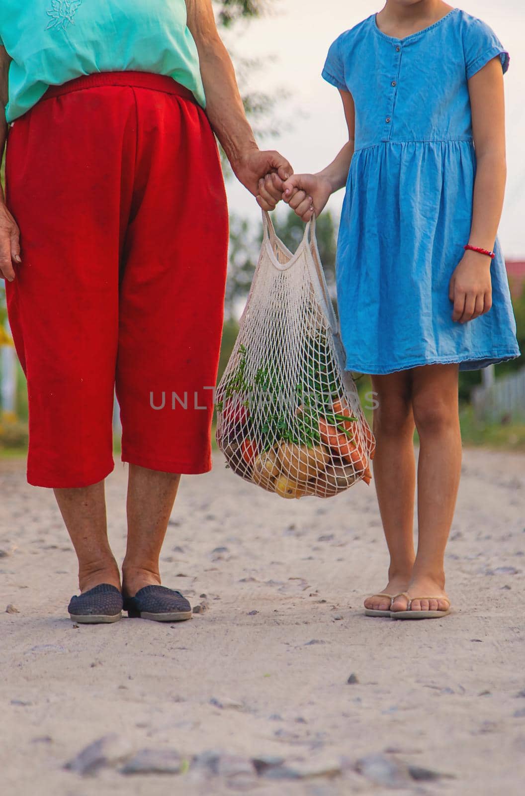 Child and grandmother carry vegetables in a bag. Selective focus. by yanadjana