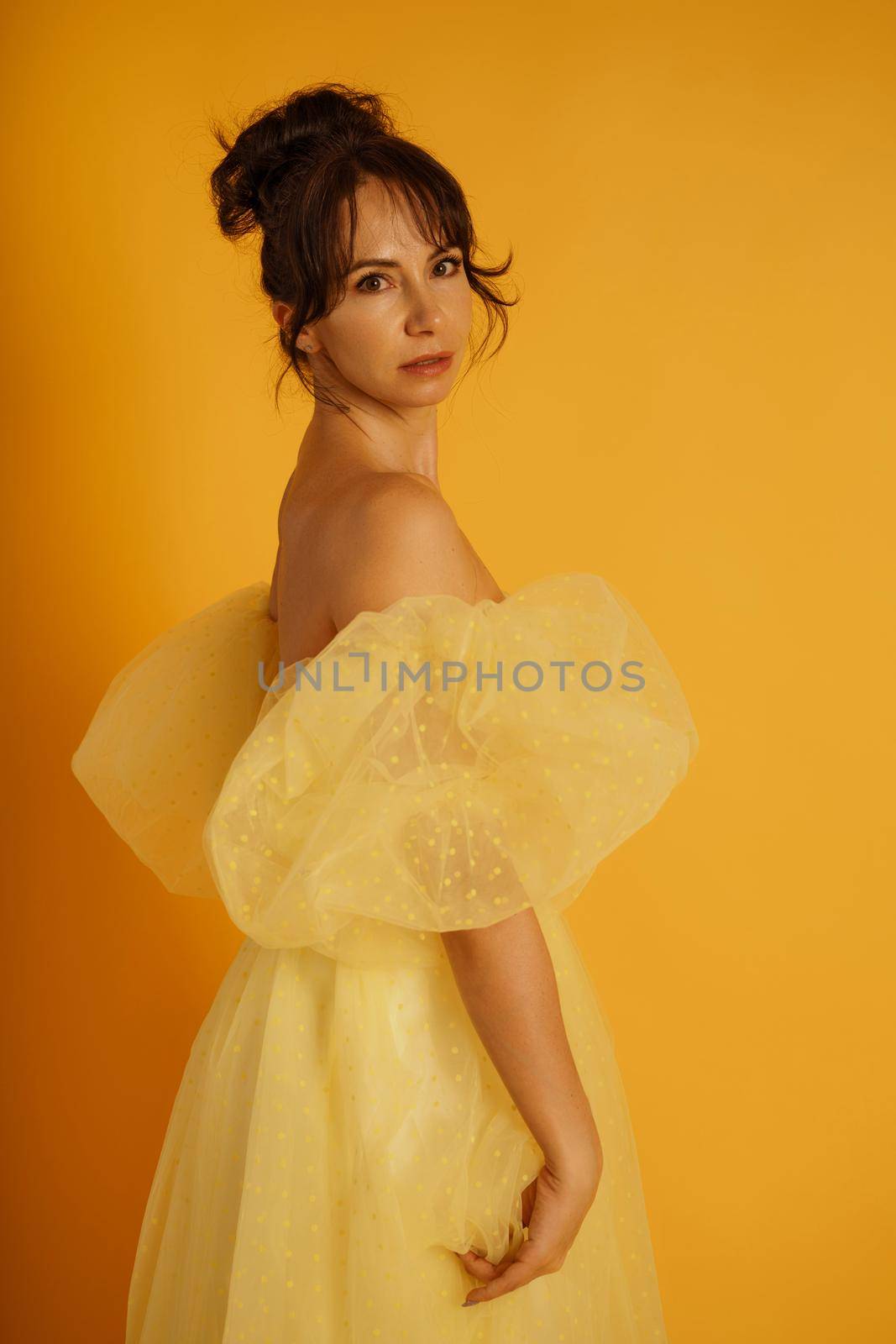 Portrait of a beautiful middle-aged woman in a yellow dress, her hair pulled up against a yellow background.