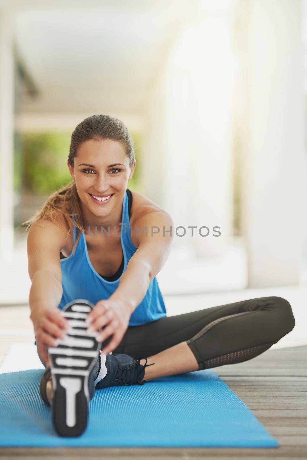 Before every workout, stretch. Portrait of an attractive young woman stretching before her workout. by YuriArcurs