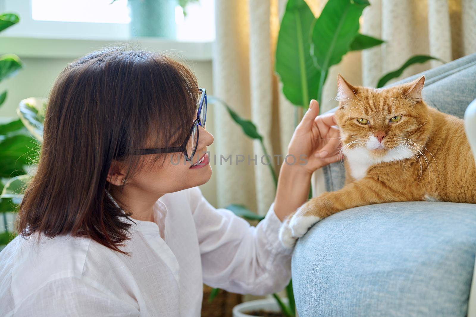 Middle aged woman talking with ginger pet cat, home interior background by VH-studio