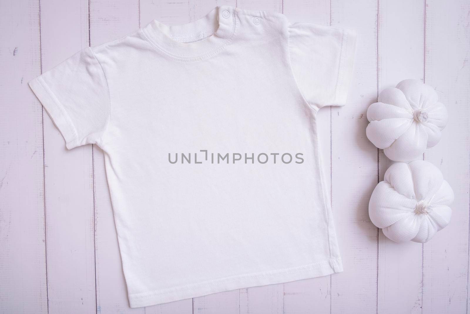 White children's t-shirt mockup for logo, text or design on wooden background with pumpkins top view.