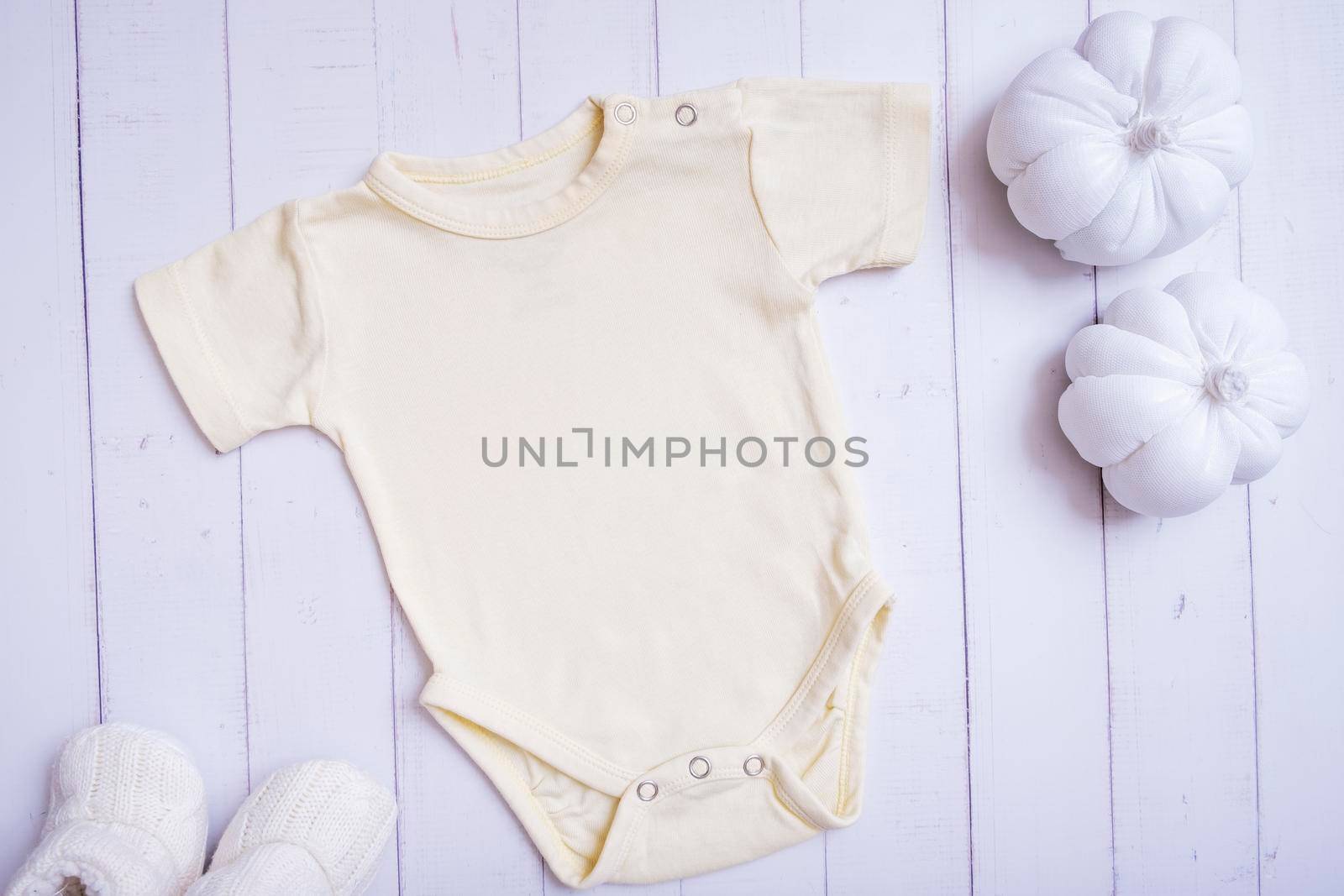 Yellow baby bodysuit mockup for logo, text or design on wooden background with pumpkins top view.