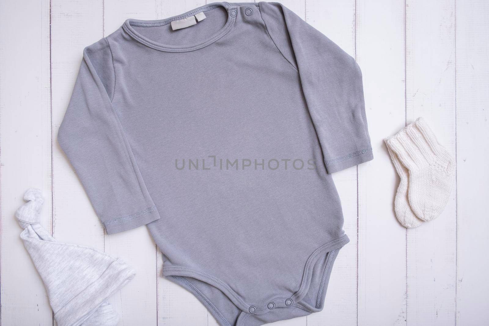 Grey baby bodysuit mockup for logo, text or design on wooden background with hat and socks top view.