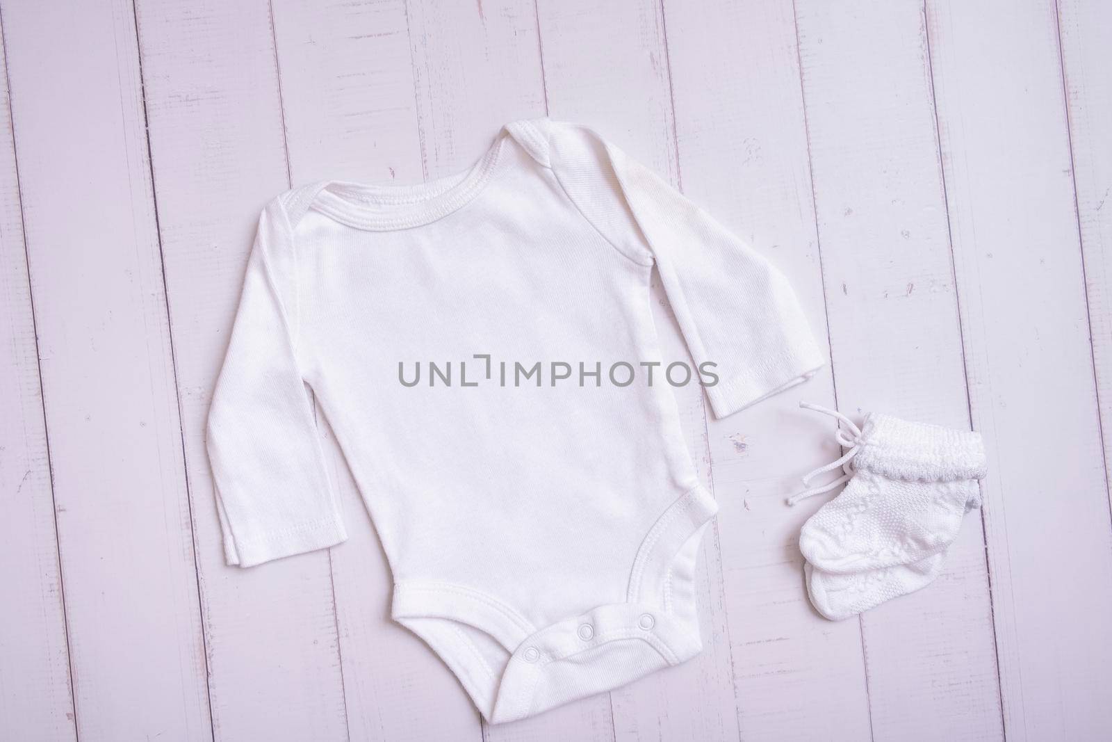 White baby bodysuit mockup for logo, text or design on wooden background top view.