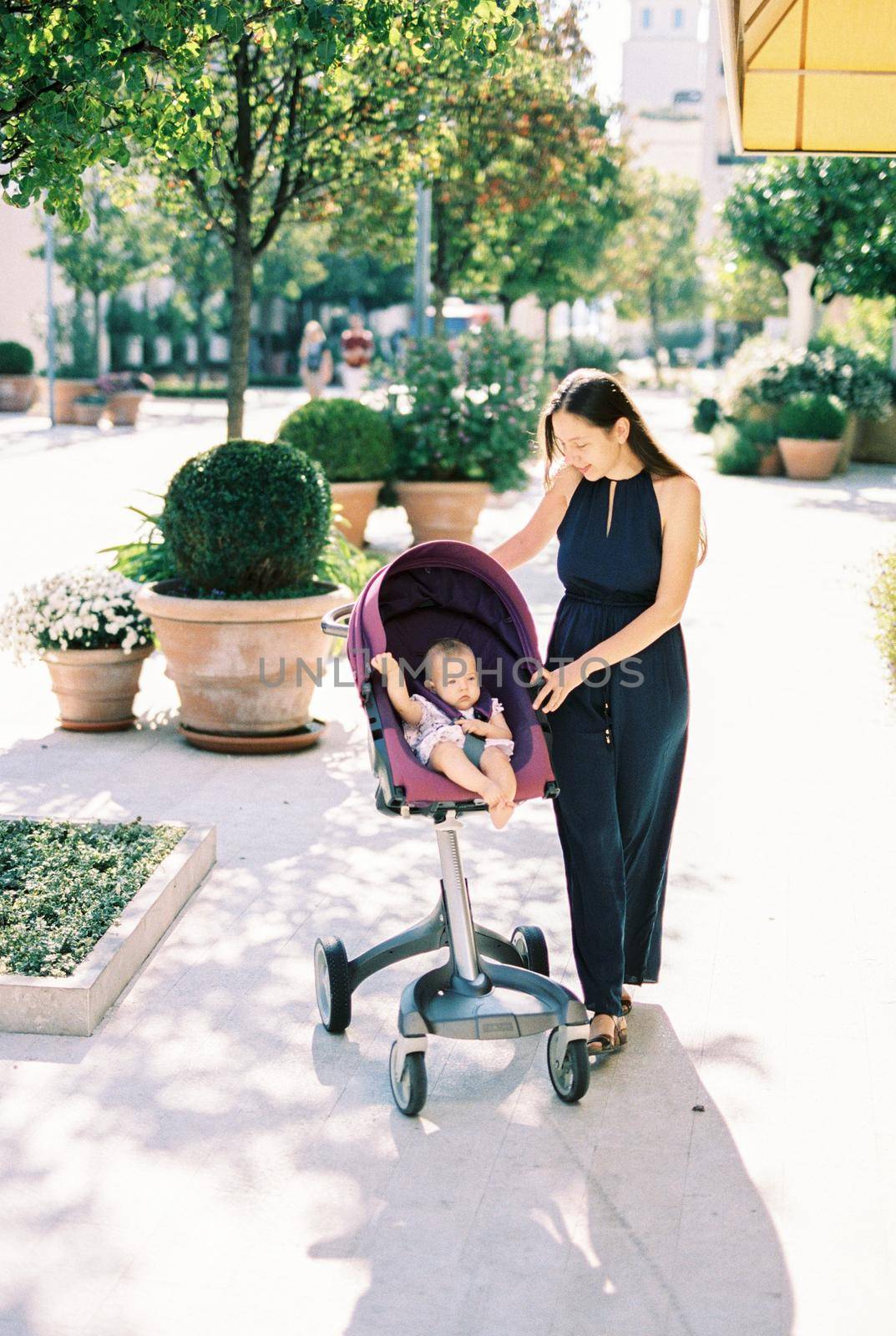 Mom stands near the stroller with the baby on the street near the flowerpots. High quality photo