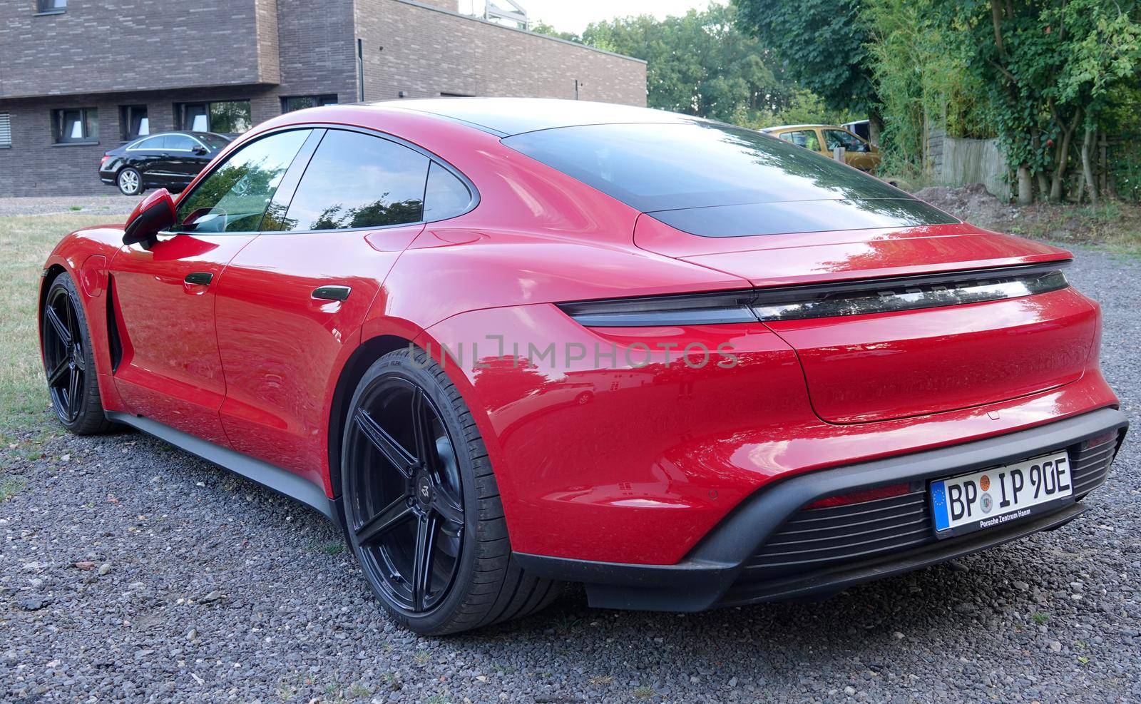 Rheine, NRW, Germany - August 24 2022 A red Porsche Taycan parked on gravel. This is an electric sedan and Porsche's first series-produced electric car