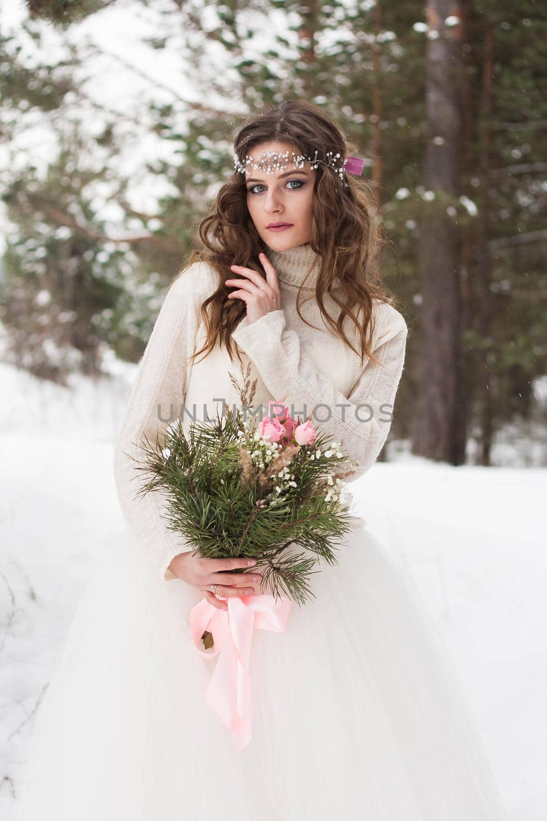 Beautiful bride in a white dress with a bouquet in a snow-covered winter forest. Portrait of the bride in nature.