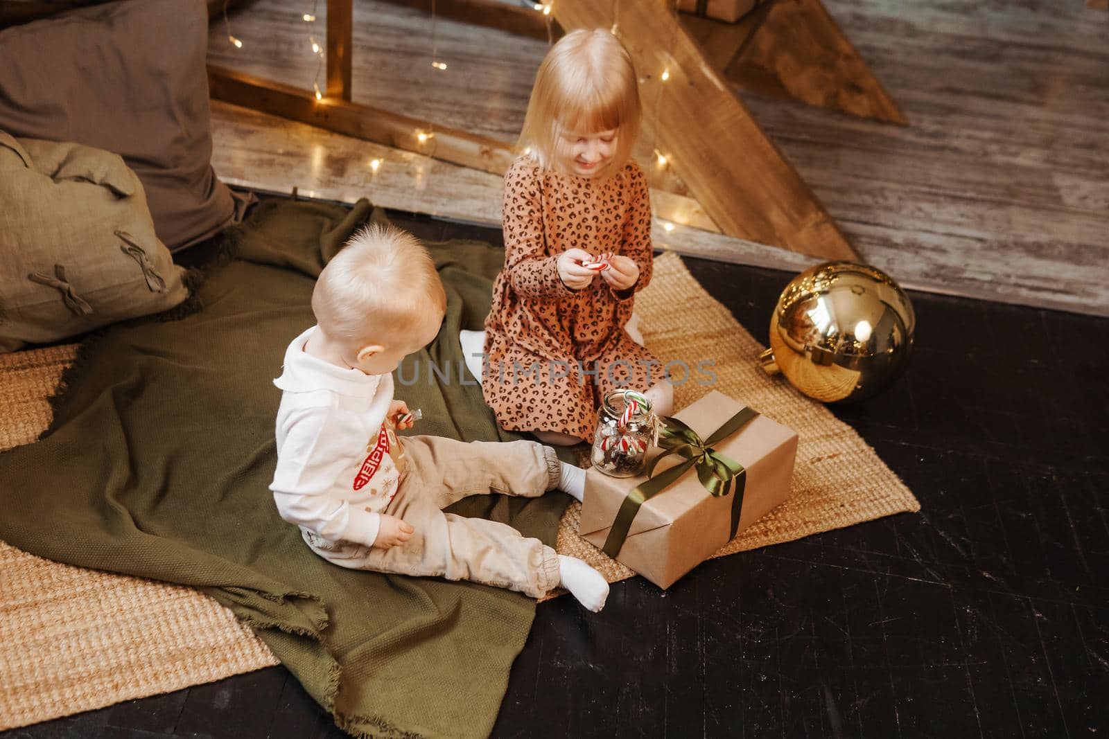Little brother and sister play on Christmas eve in a beautiful house decorated for the New Year holidays. Children are playing with a Christmas gift. Scandinavian-style interior with live fir trees and a wooden staircase.