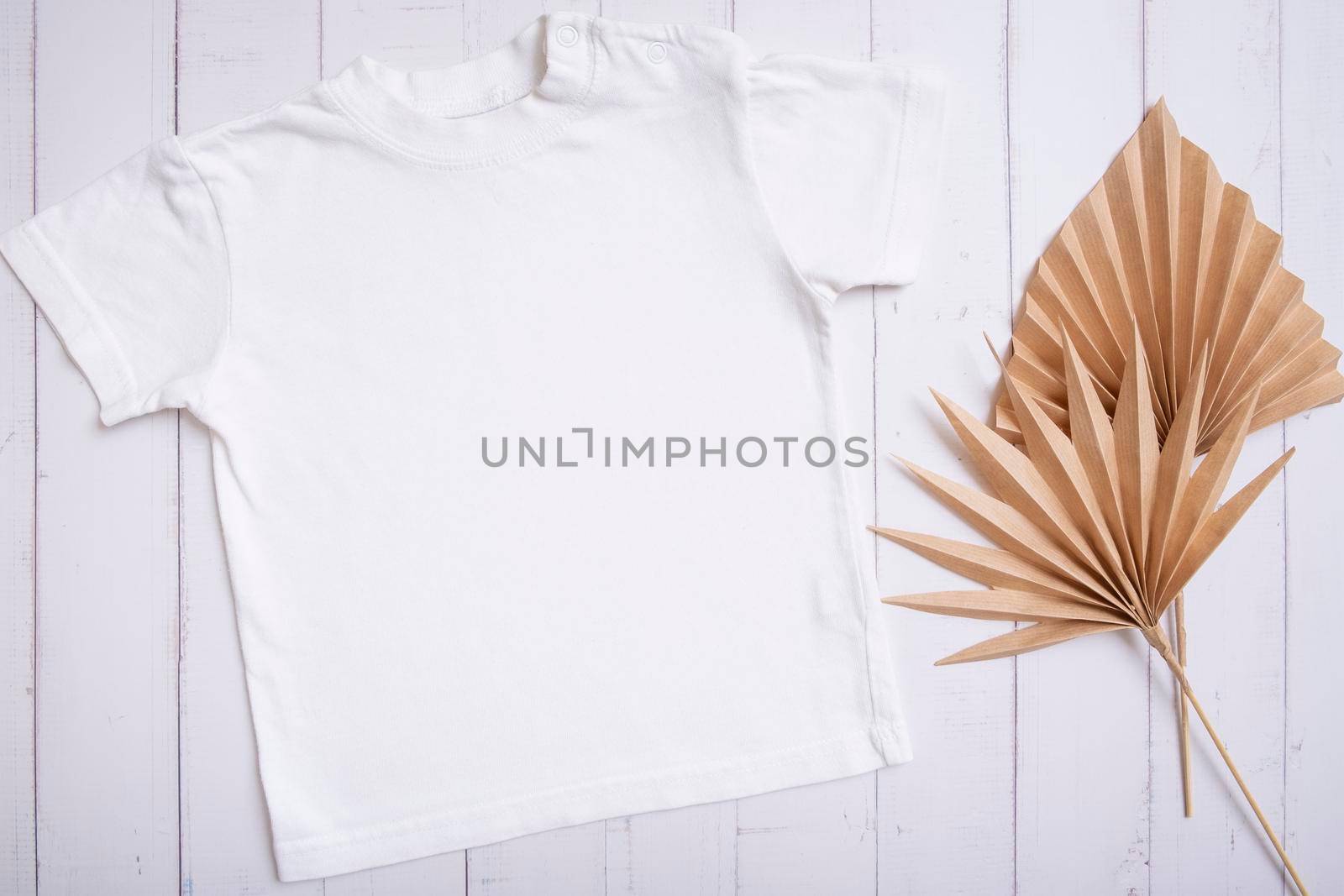 White children's t-shirt mockup for logo, text or design on wooden background with palm leaves top view.