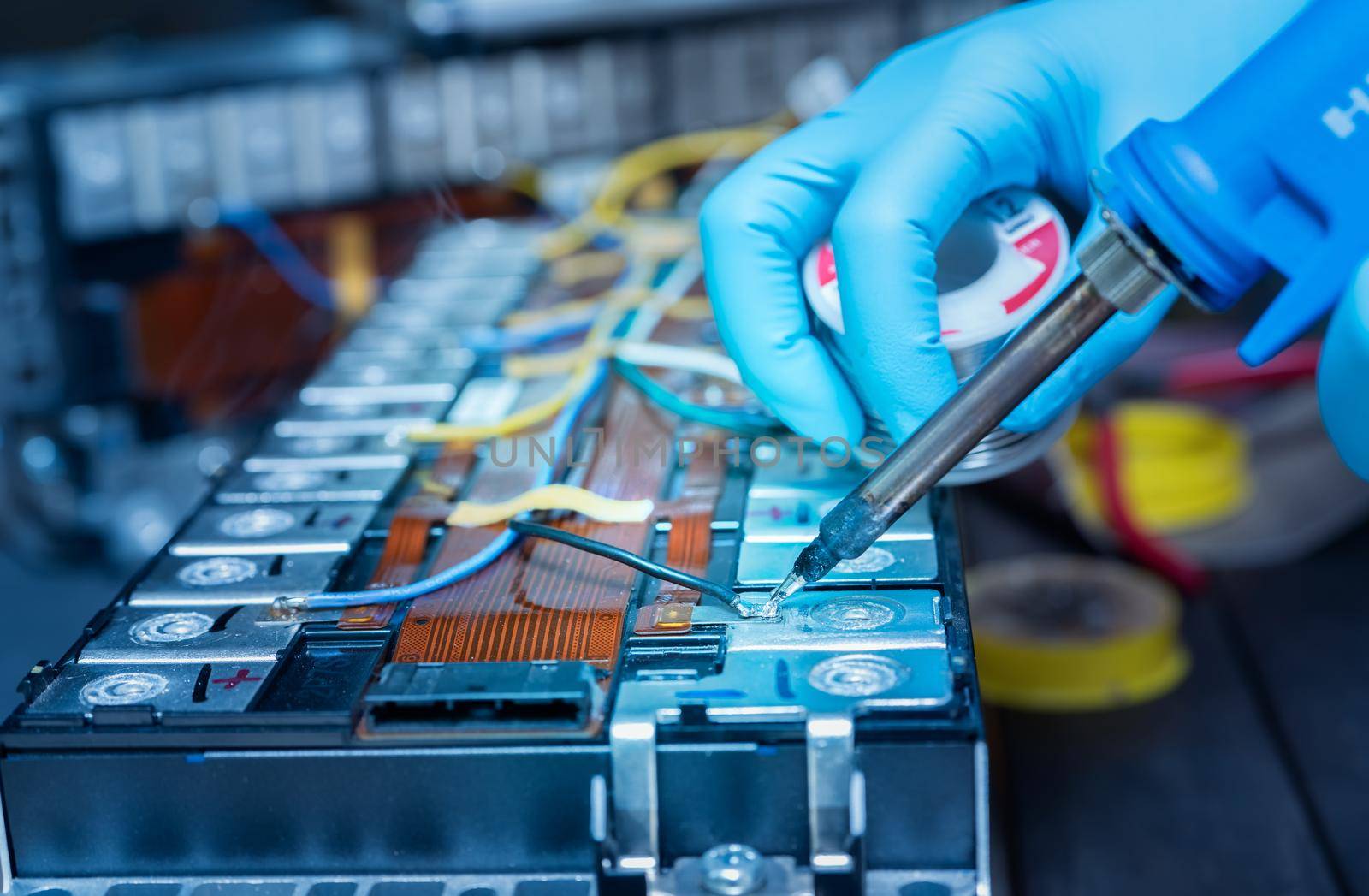 Technician use soldering iron to solder metal and wire of lithium-ion rechargeable battery. Repair module of Li-ion battery. Engineer hand holds soldering iron and tin-lead to solder electronic board.