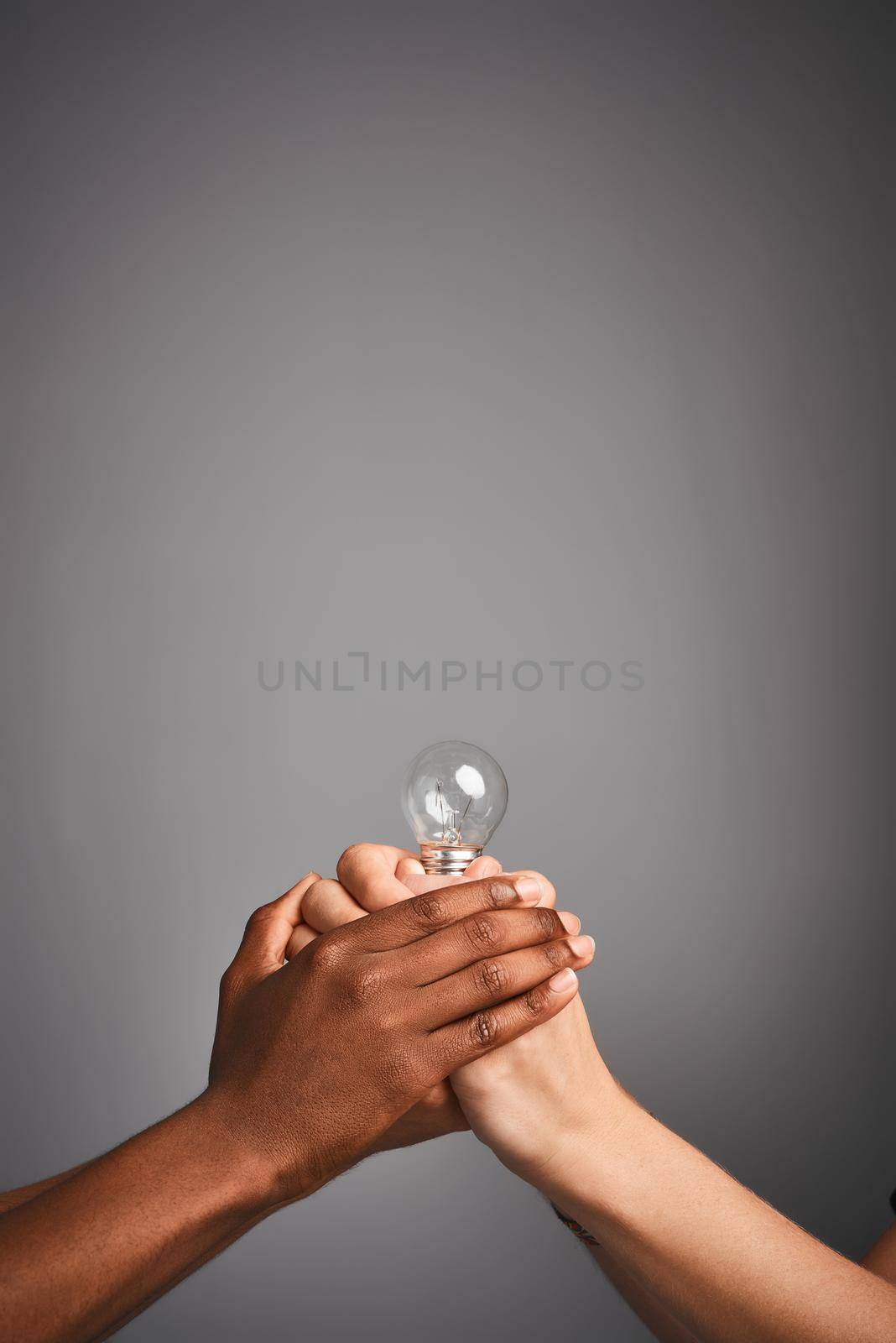 Light up someone elses day. Studio shot of unidentifiable hands holding a light bulb against a gray background. by YuriArcurs