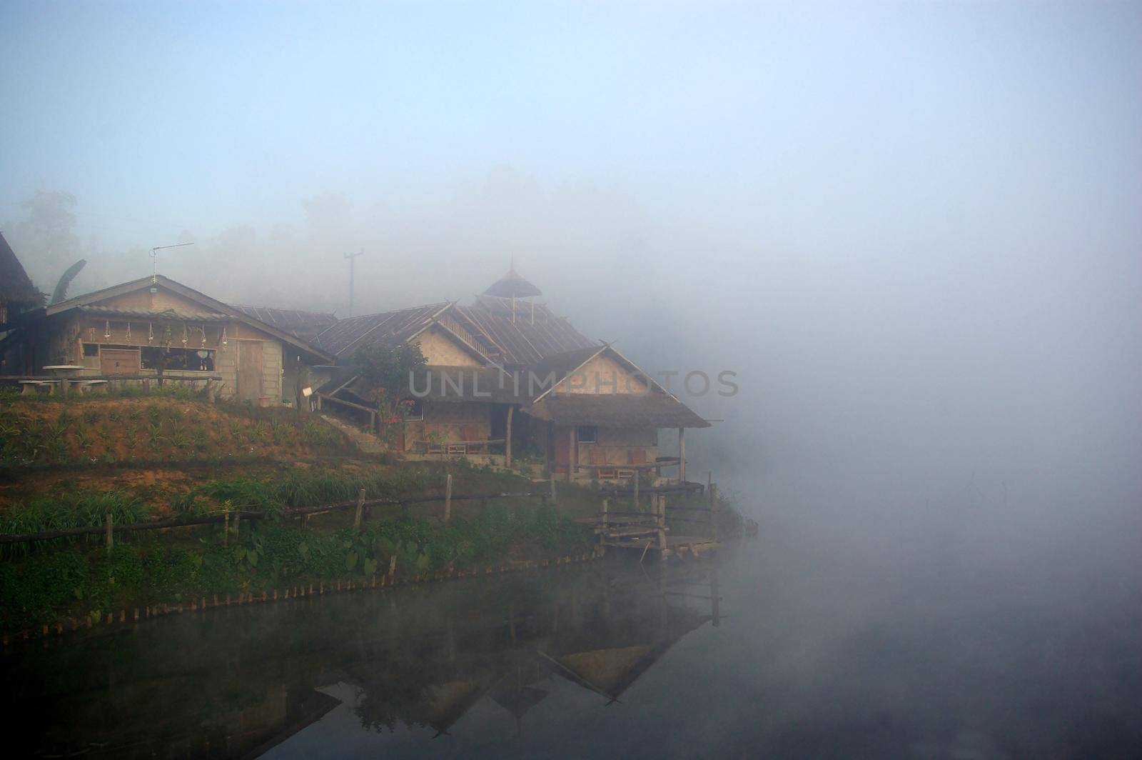 wooden house in the morning mist and the lake view in the countryside by Satakorn