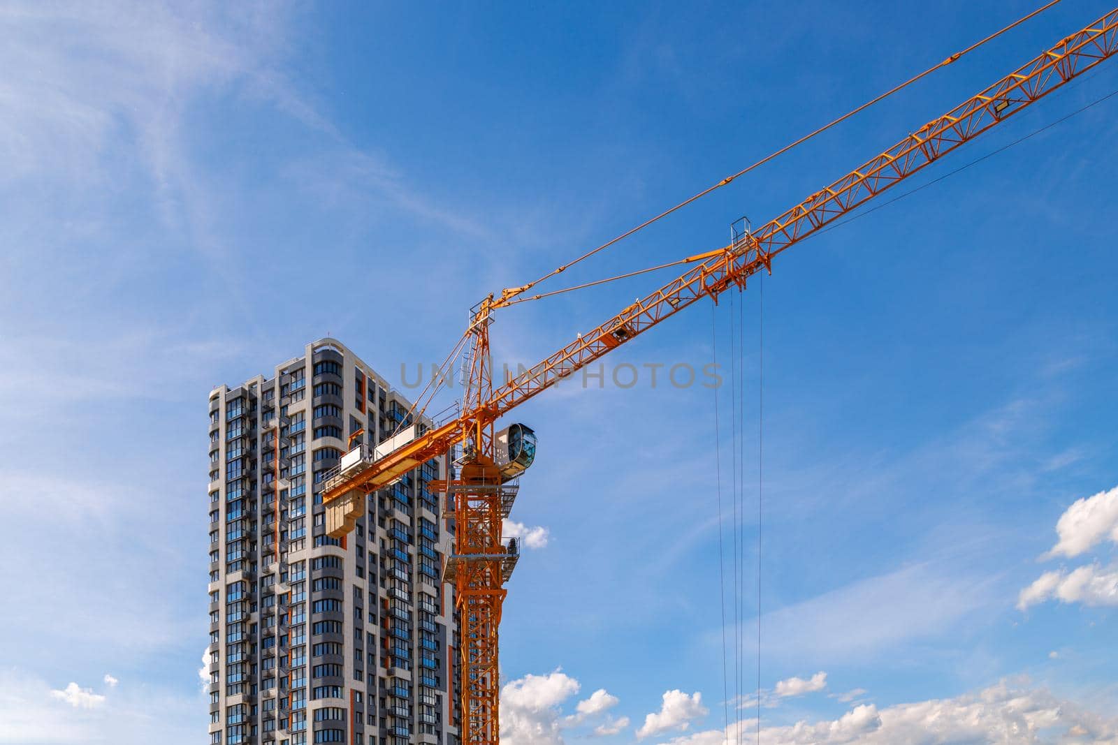 freshly built high rise apartment building near yellow crane on blue sky background with thin feathery clouds.