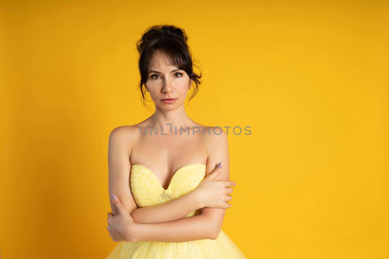 Portrait of a beautiful middle-aged woman in a yellow dress, her hair pulled up against a yellow background by Matiunina