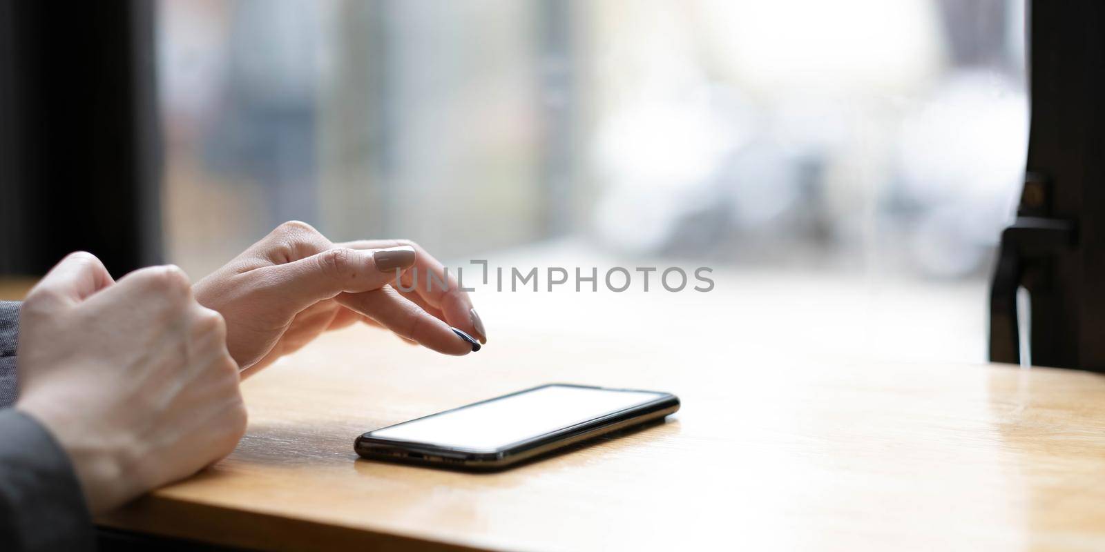 Woman holding phone with blank screen in hand on street view from window background.