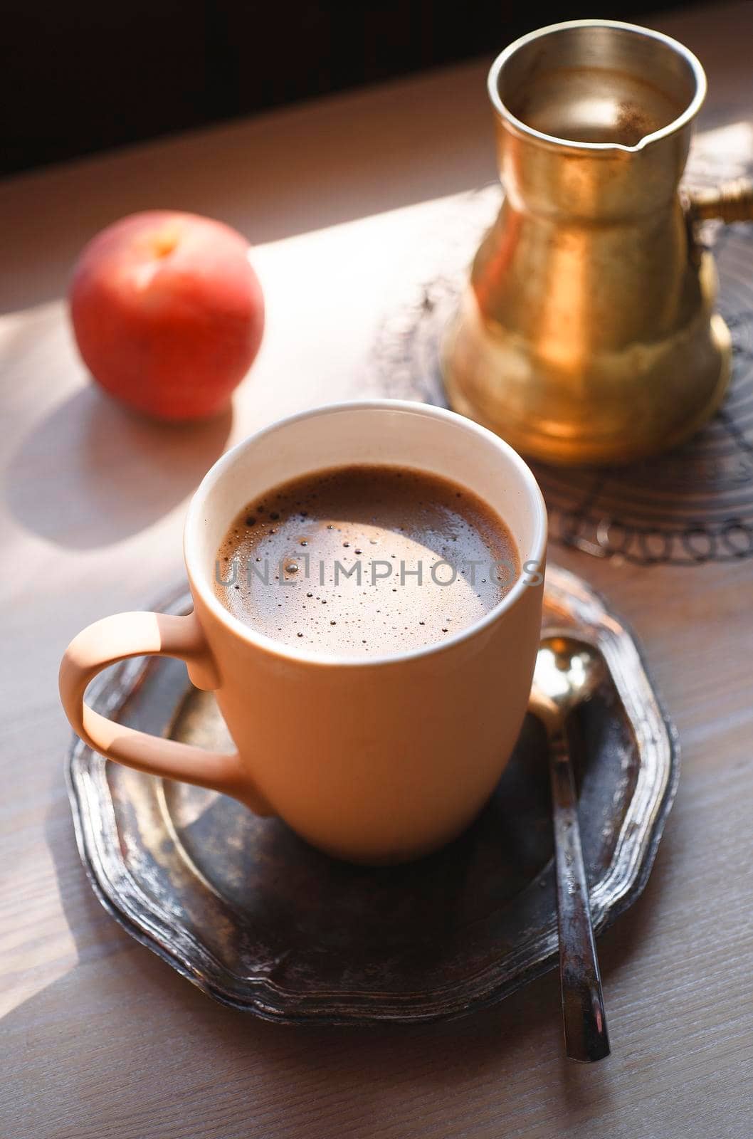 A cup of coffee on vintage metal plate with yellow copper cezve and a peach on white wooden table, summer morning concept, selective focus.