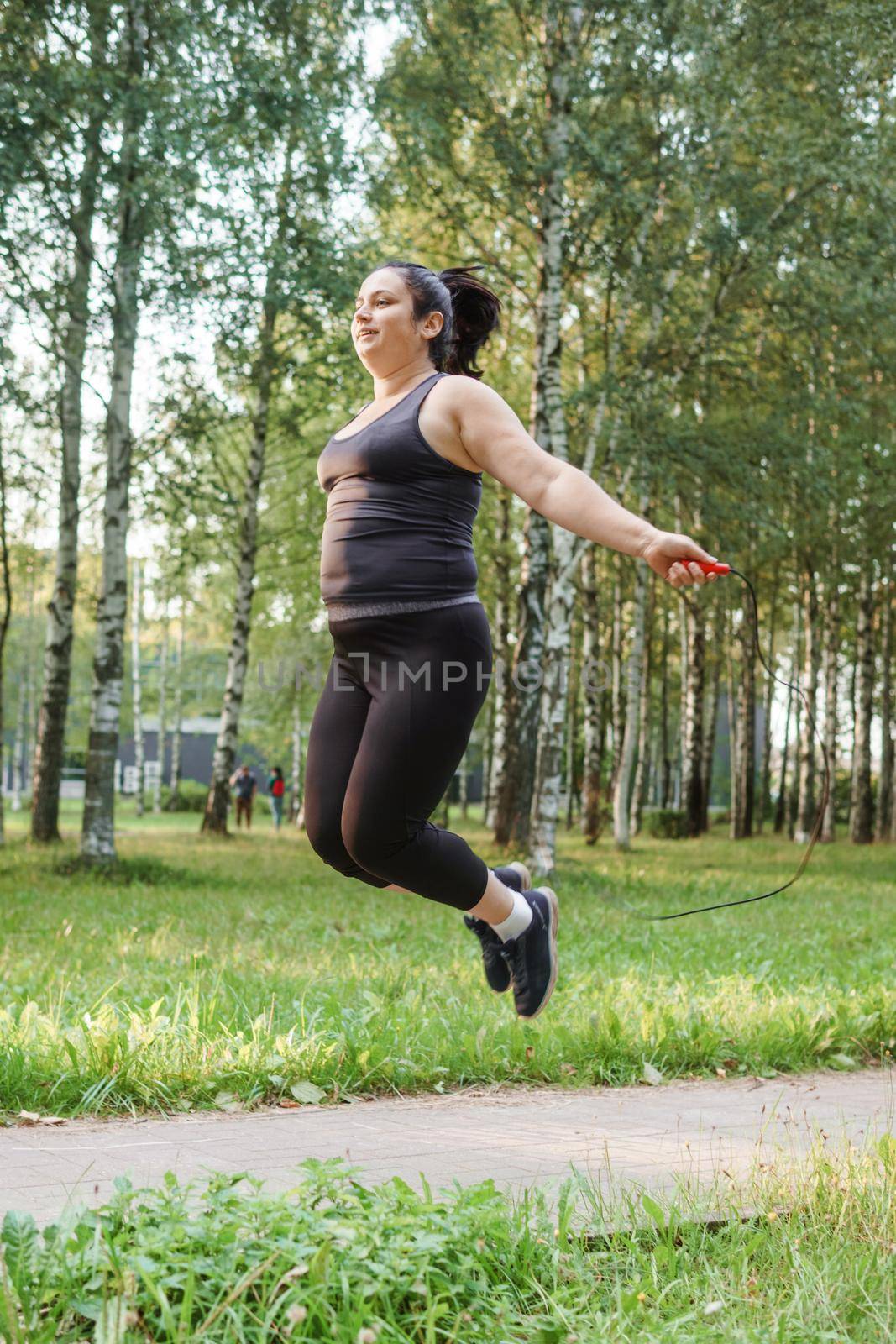 A charming brunette woman plus-size body positive practices sports in nature.