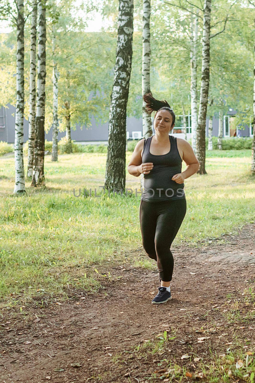 A charming brunette woman plus-size body positive practices sports in nature.