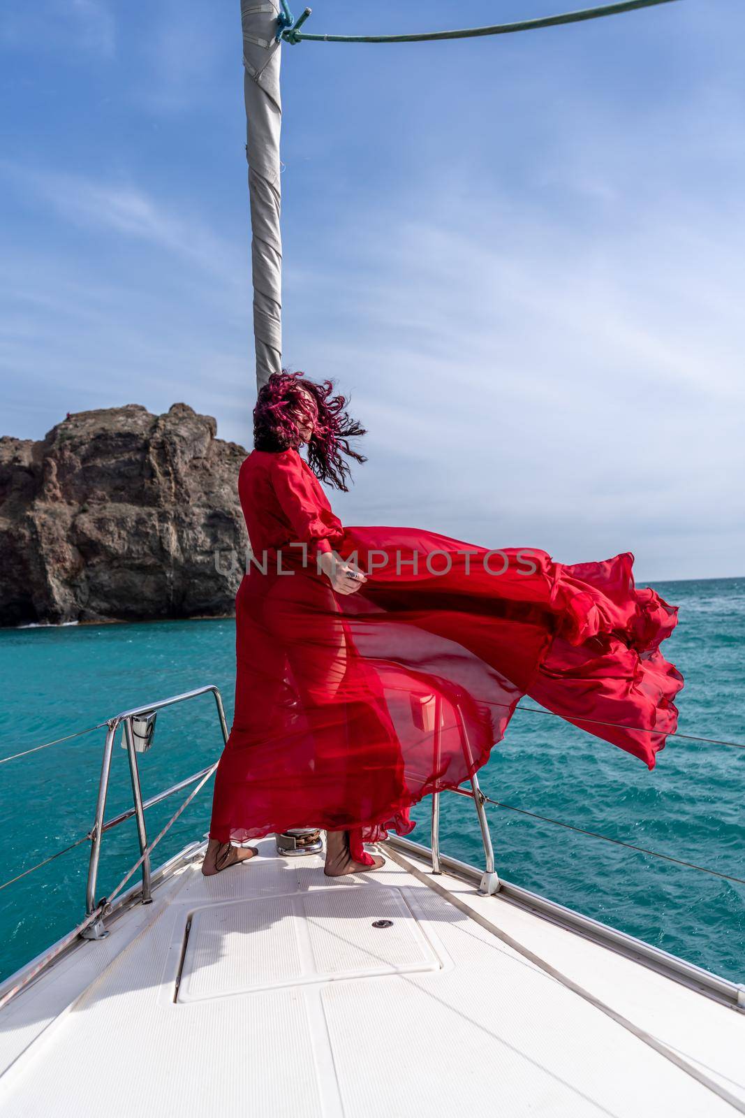 Attractive middle-aged woman in a red dress on a yacht on a summer day. Luxury summer adventure, outdoor activities