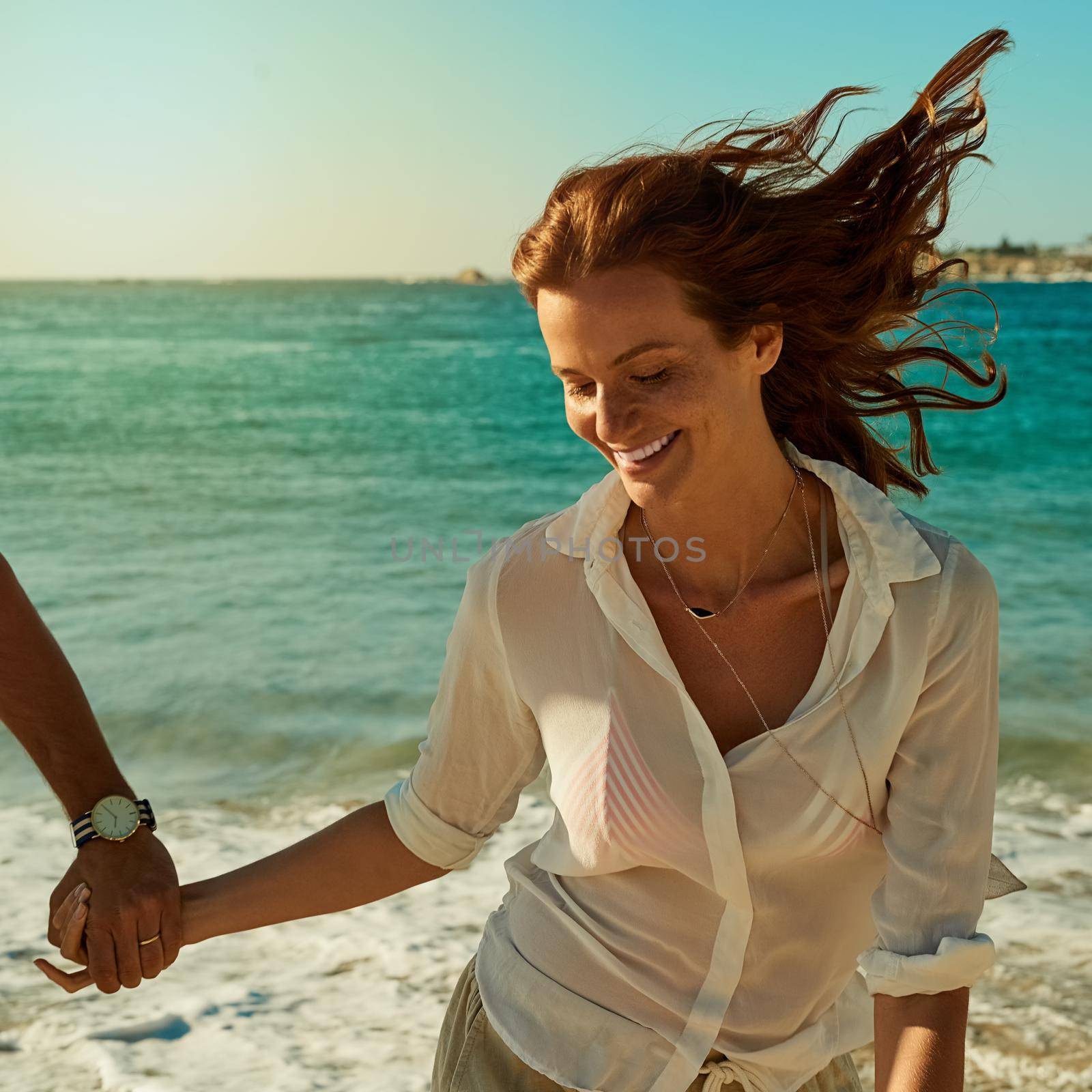 Carefree living is what the seasons all about. a happy young woman running along the beach with her boyfriend. by YuriArcurs