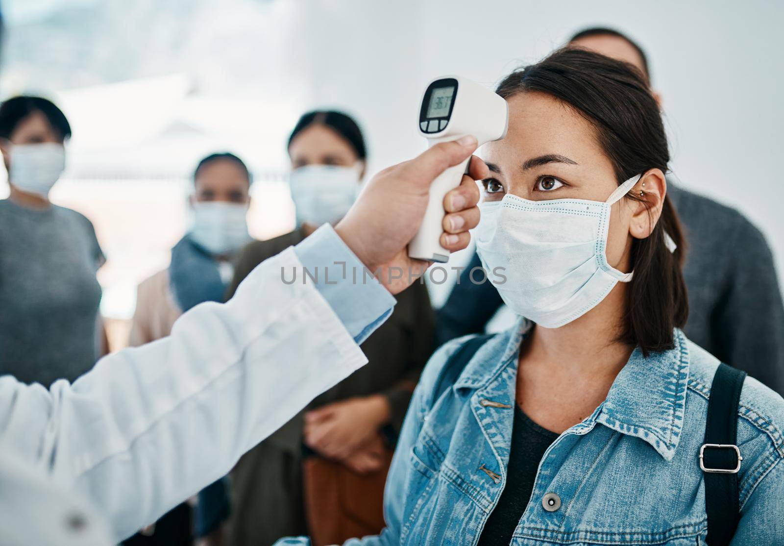 Covid screening with a female tourist in a mask having her temperature taken with an infrared thermometer while waiting to board in an airport. Travel restrictions during the corona virus pandemic.