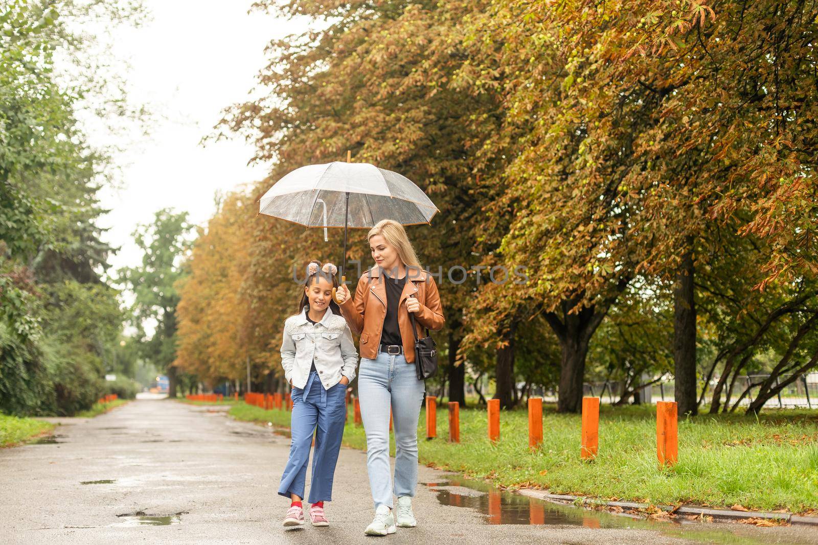 Cheerful mother and her little daughter having fun together in the autumn background under the umbrella. Happy family in the fall background.