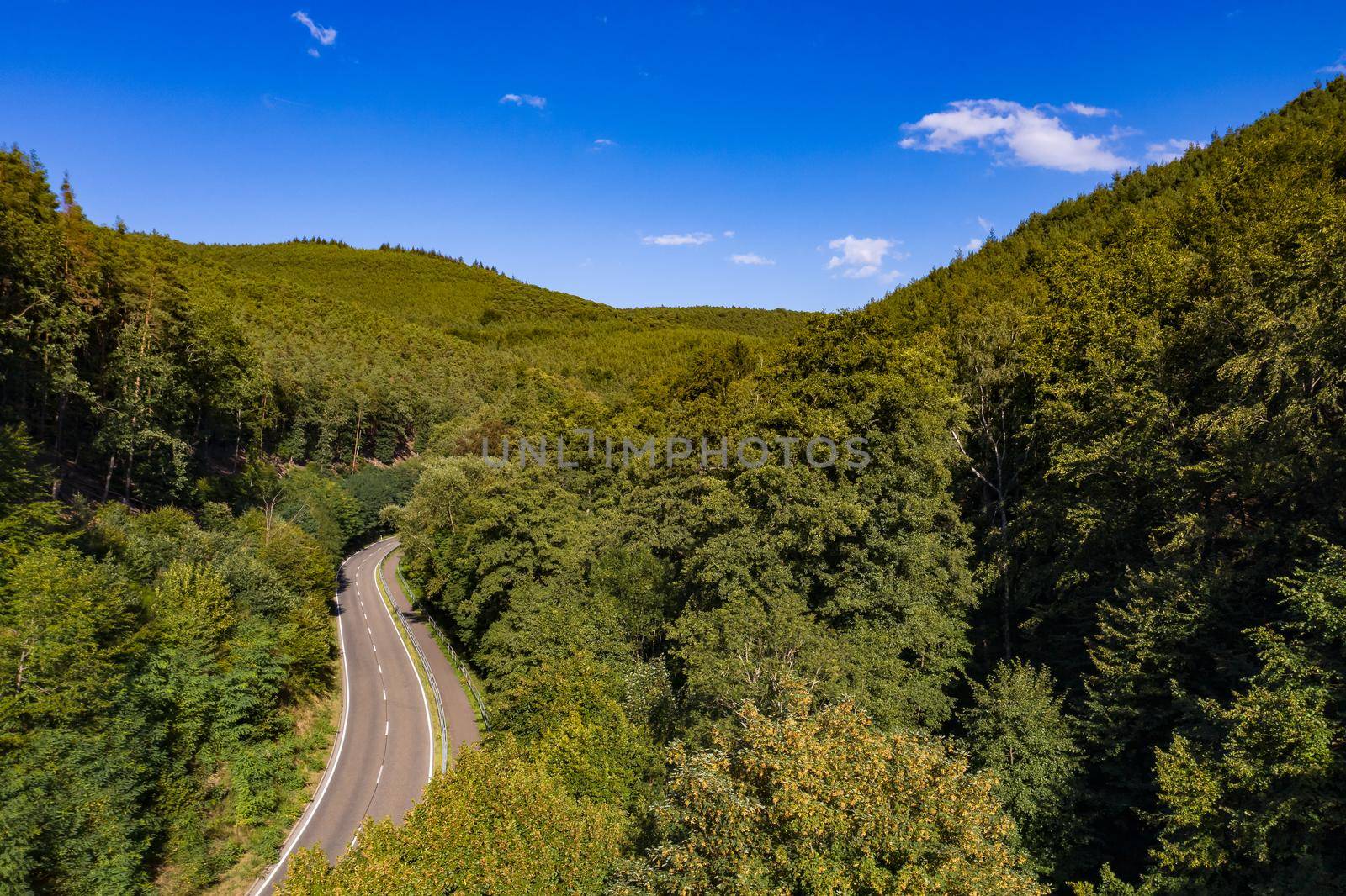 Aerial view of a mountain road with a bike path through a healthy European mixed forest