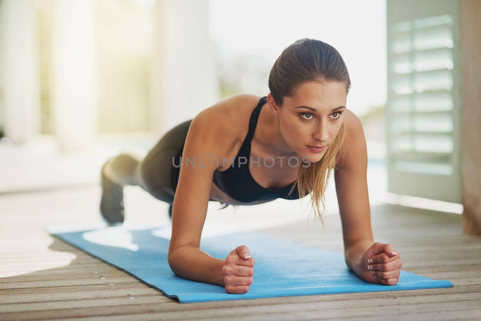 Building upper body strength. an attractive young woman planking on her patio. by YuriArcurs