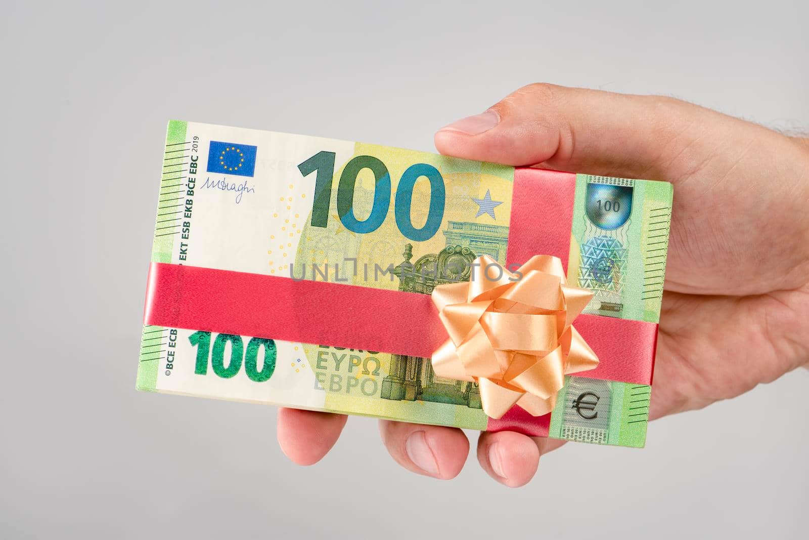 Gift of money. A pack of 100 euro bills in a man's hand. Money gift concept for birthday or christmas. Give euro with gift ribbon.