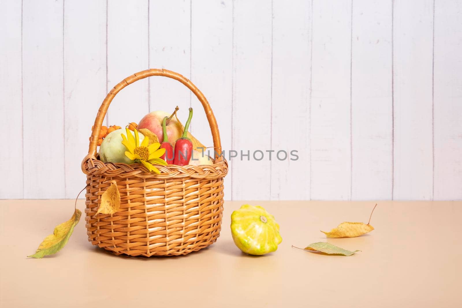 Autumn harvest basket with corn, apples, zucchini and peppers on a wooden background decorated with autumn flower.