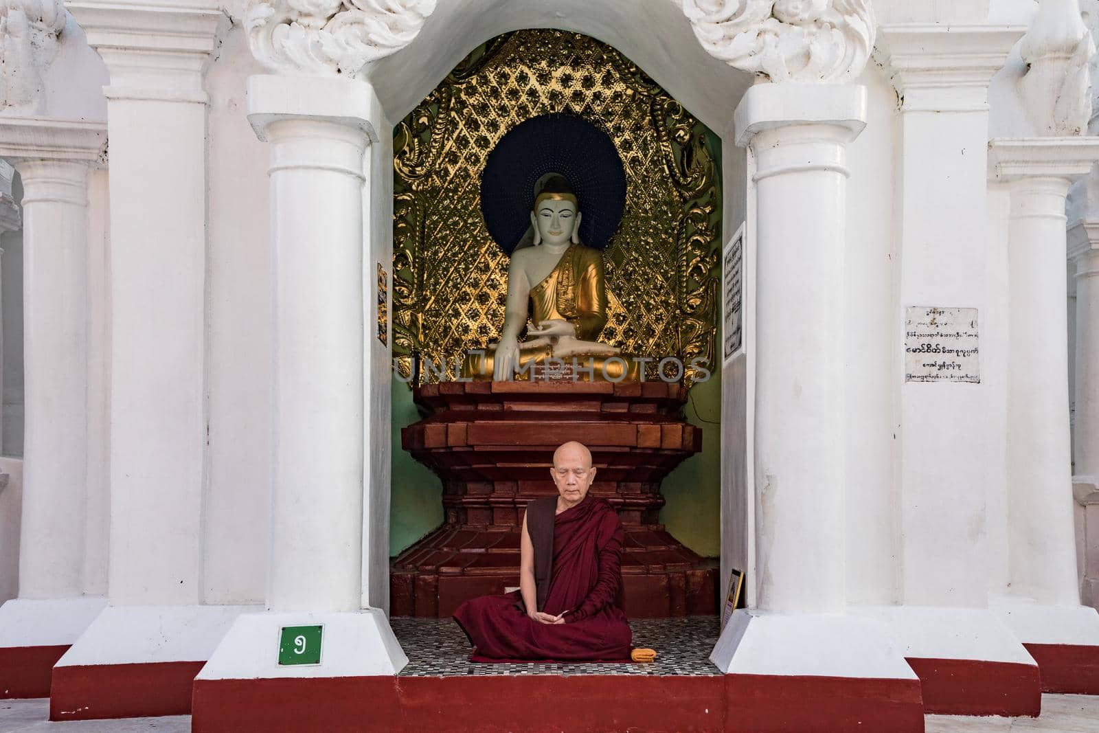 A monk meditating in front of a Buddha statue in Yangon