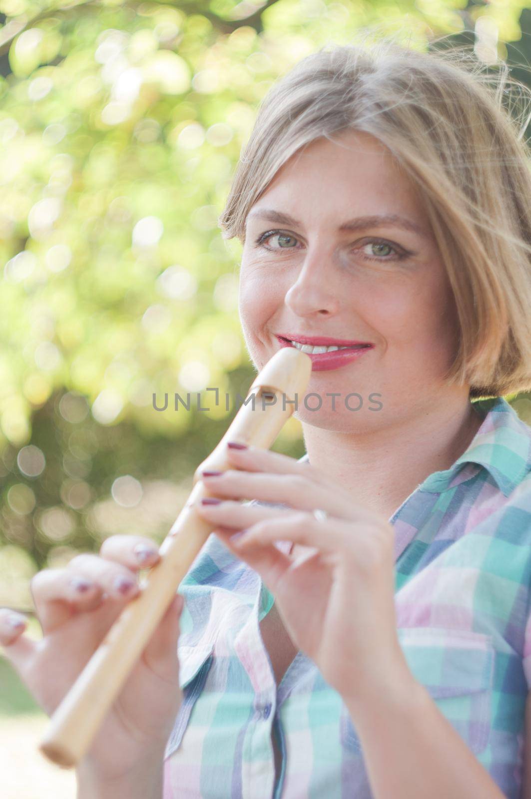 young beautiful caucasian girl dressed in pin-up style plays the flute and smiles, bright sunny day. High quality photo