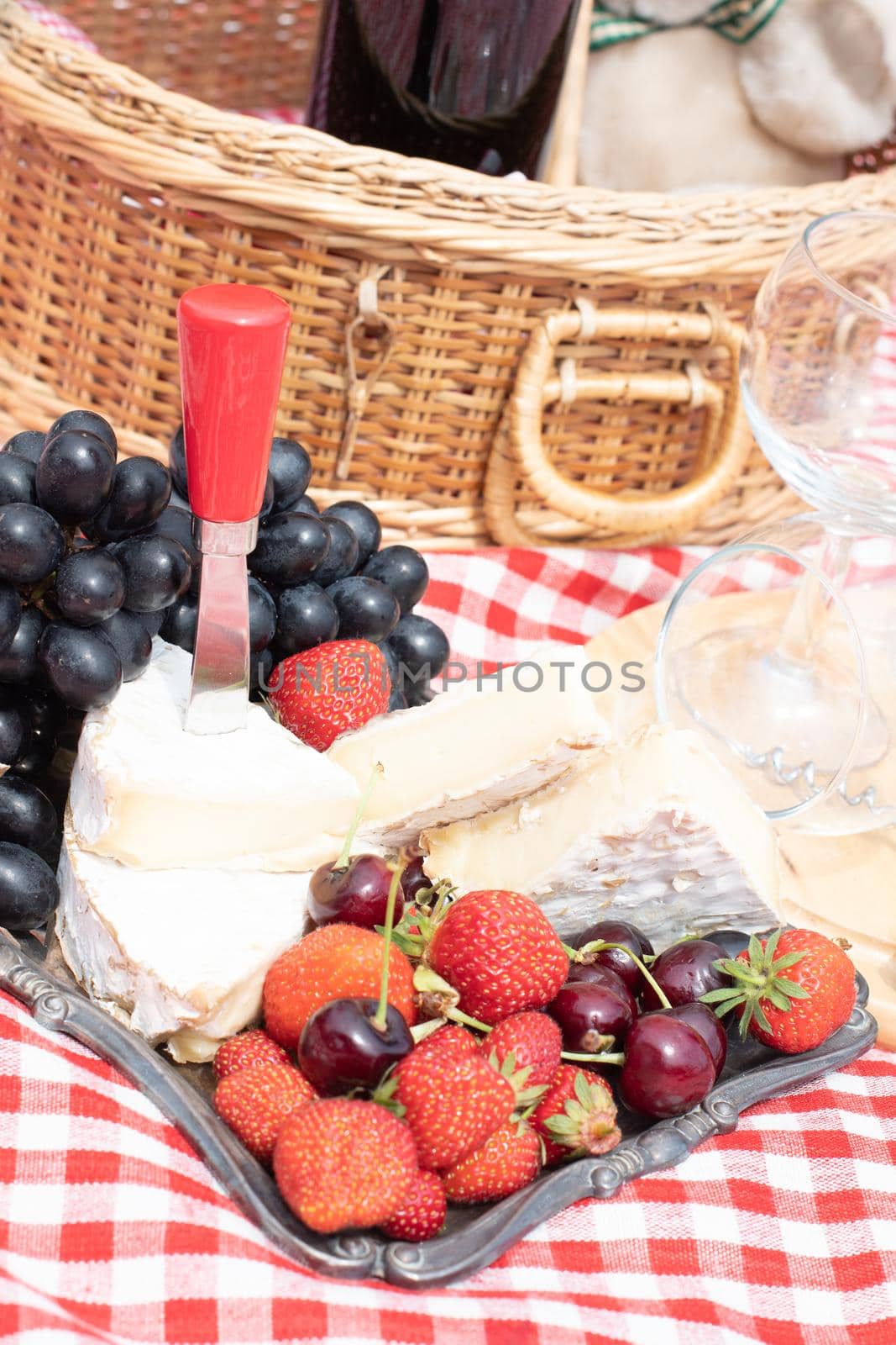 summer picnic on a green lawn with red wine, cheese and fresh berries, grapes by KaterinaDalemans