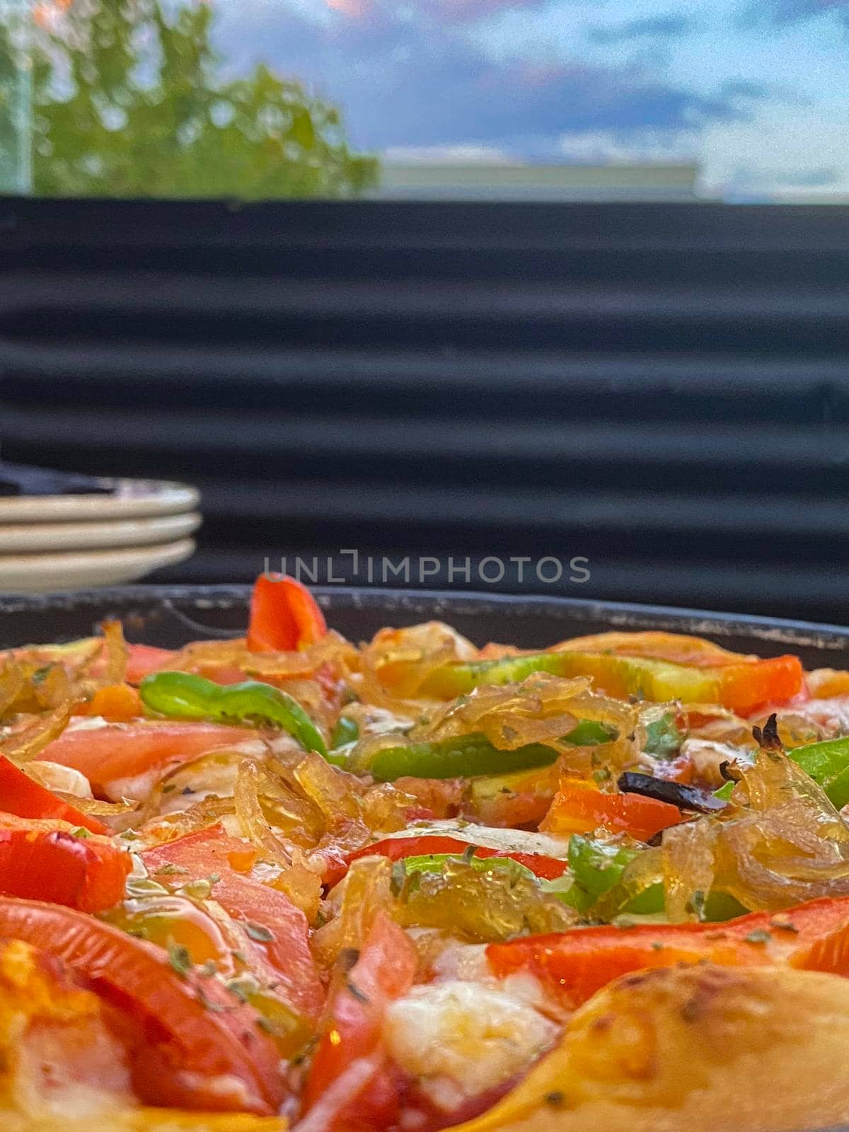 Close up of colourful pizza with onion pepper and tomato.plates in the background